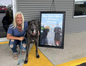 Kiaya Martin and her Great Dane, Bullet, pose next to a framed image of her book cover.