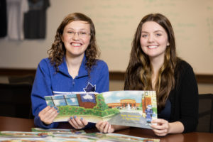Two women pose with a copy of the children's book "Sam Becomes a Sycamore."