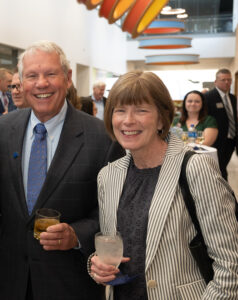 Mike Alley, a white man with short gray hair, poses with his wife, Amy Alley, a white woman with shoulder-length light brown hair. Amy wears a black-and-white striped jacket and a dark blue blouse. Mike wears a dark suit jacket over a light blue dress shirt and a blue tie.