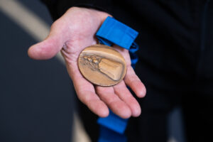 A person's hand holding a medal carved with a bobsled.