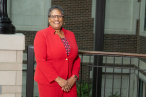 Mary Howard-Hamilton, a Black female professor, wears a red pantsuit. She poses in front of a railing in the atrium of University Hall in the Bayh College of Education.